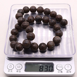 Macro view of 12mm brown gemstone beads on a digital scale showing 83g weight