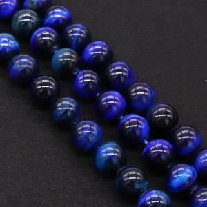 Macro shot of polished blue tiger eye beads with natural cat-eye effect on black texture