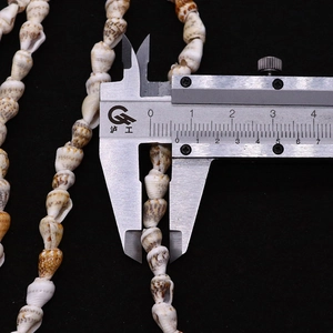Detail view of 7mm natural shell beads showing speckled texture and precision measurement
