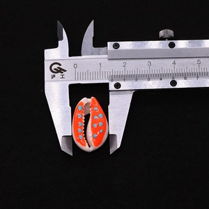 Detailed view of the 15mm orange and white patterned shell bead being measured
