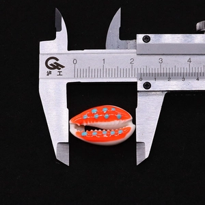 Macro shot of a 25mm orange and white cowrie shell bead measured with a caliper tool