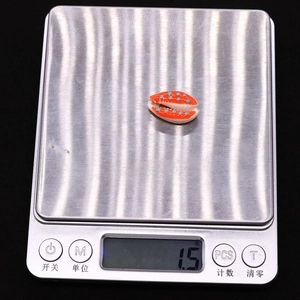 Detailed view of an orange seashell bead with blue dots on a scale weighing 1.5 grams