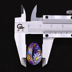 Macro shot of a painted floral cowrie shell bead measured with a caliper at 1.9cm width
