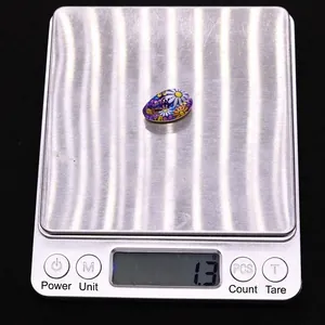 Detailed view of flower pattern bead on a digital scale showing 1.3g weight