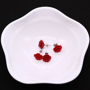 Two pairs of red synthetic coral rose earrings on a white ceramic dish