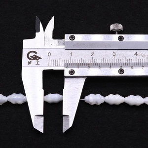 Macro shot showing 13mm oval shell bead size being measured with a digital caliper