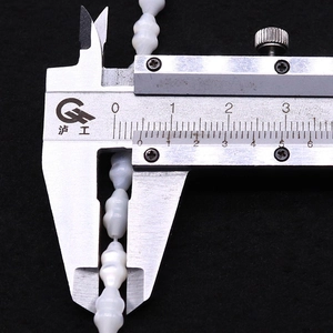 Macro view of a digital caliper measuring an 11mm white spindle-shaped shell bead