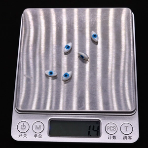Macro detail of five evil eye shell beads on digital scale showing 1.4g weight
