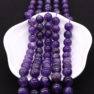 Perles rondes d'améthyste violette naturelle sur plat de coquillage blanc avec fond noir contrasté