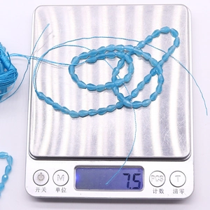 Macro view of light blue faceted teardrop beads on a digital scale weighing 7.5 grams
