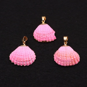 Gros plan de trois pendentifs en coquillage rose avec bordure dorée sur fond noir