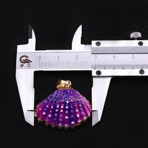 Détail d'un pendentif coquillage violet avec bords dorés mesuré par un étrier