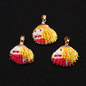 Vue détaillée de trois pendentifs en coquillage colorés à bord doré sur fond noir