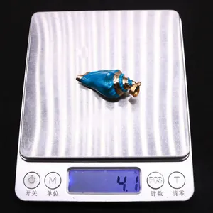 Detalle de colgante de caracola esmaltada azul de 4,1g con borde dorado en una báscula