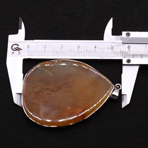 Macro detail of teardrop agate pendant measured with silver caliper on black background