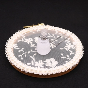 Detail of frosted white stone perfume bottle pendant with silver chain on lace decor