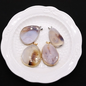 Natural teardrop agate stone pendants with gold and silver plated edges on a white plate