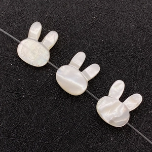 Three rabbit-shaped white mother of pearl shell beads with iridescent glow on black texture