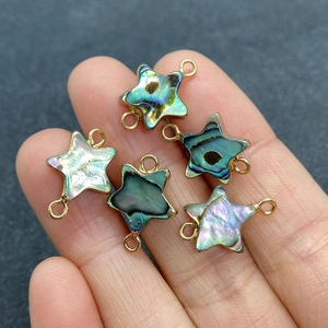 Star-shaped abalone shell connectors with gold frames held in hand for jewelry making