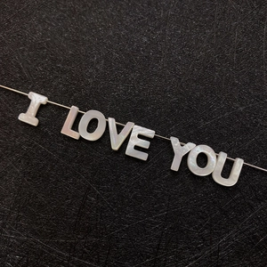 Macro detail of natural mother of pearl alphabet beads spelling I LOVE YOU on black fabric