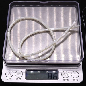 Détail macro de perles cylindriques en nacre blanche pesant 8,6g sur une balance