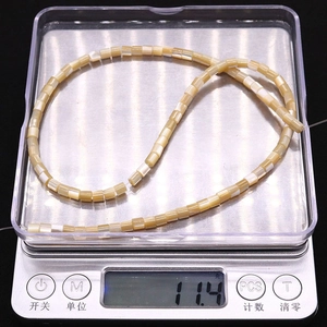 Macro detail of cylindrical natural shell beads showing weight on digital scale for DIY jewelry