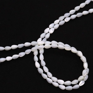 Macro shot of white teardrop shell beads with iridescent luster on a dark background