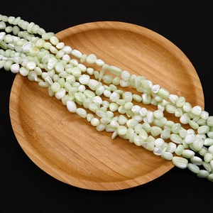 Detailed close-up of irregular light green and ivory natural sea shell beads in a wooden tray