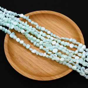 Macro detail of irregular light blue sea shell beads arranged on a wooden tray