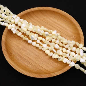 Close-up of irregular natural shell beads with pearlescent luster in a wooden tray