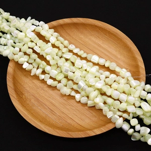 Close-up of irregular light green shell beads displayed in a rustic wooden bowl