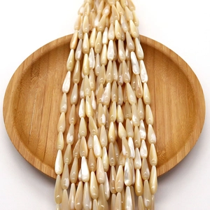 Natural champagne shell teardrop beads with pearlescent luster on round wooden tray