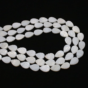 Macro shot of white mother-of-pearl leaf-shaped beads with detailed carvings on black background