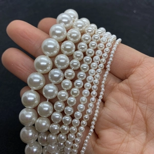 Polished white faux pearl strands in various sizes held by hand for jewelry DIY
