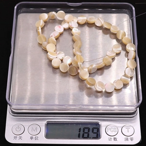 Detailed view of flat round mother of pearl beads on electronic scale showing 18.9g weight