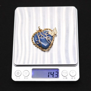 Macro view of heart-shaped lapis lazuli pendant with gold wire wrap and butterfly charm