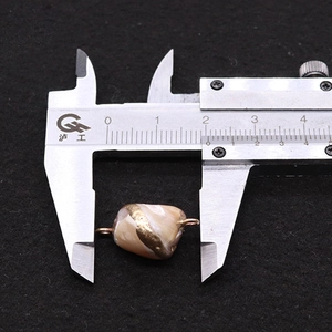 Caliper measuring a 18mm natural sea shell tooth pendant connector with gold trim