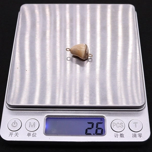 Close-up of a 2.6g natural shell connector pendant being weighed on a digital scale