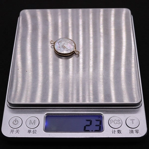 Macro shot of a 2.3g natural shell pendant with gold edges on an electronic scale