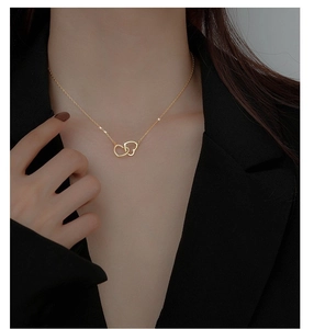 Détail d'un collier double cœur doré porté par un mannequin en vêtements noirs