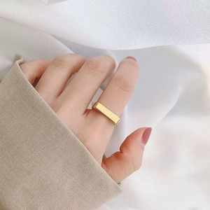 Close-up of a minimalist golden square signet ring worn on a hand against white fabric