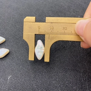 Detail view measuring 9mm white baroque pearl with iridescence using a brass caliper