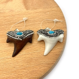 Vista ravvicinata di due ciondoli a dente di squalo con resina e strass brillanti