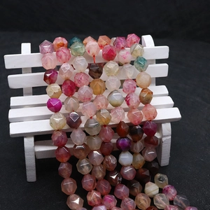 Faceted dragon vein agate beads in pink and orange tones displayed on a white wood bench