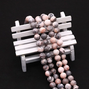 Close-up of polished pink zebra stone beads with natural grey patterns on black background