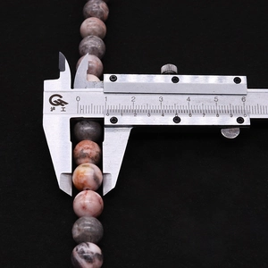 Macro shot of natural pink zebra stone bead being measured with a metal caliper