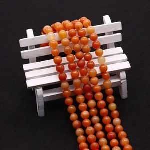 Strands of smooth orange aventurine beads draped on a miniature wooden chair backdrop