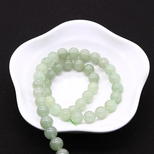 Polished light green aventurine round beads displayed in a white petal-shaped ceramic dish