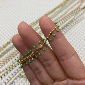 Detail of a thin gold chain featuring green drip oil bead charms and multi-color variants