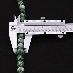 Makroaufnahme einer grünen Natursteinperle, die mit einem Messschieber 8mm Durchmesser misst